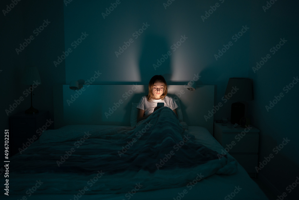 A person reading on a phone in a dark bedroom at night.